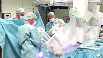 Ein chirurgisches Team in blauen OP-Kitteln führt eine Operation mit einem robotergestützten System durch.