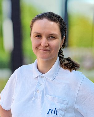 Eine Person mit einem weißen Poloshirt mit der Aufschrift "srh" steht mit verschränkten Armen und lächelt.