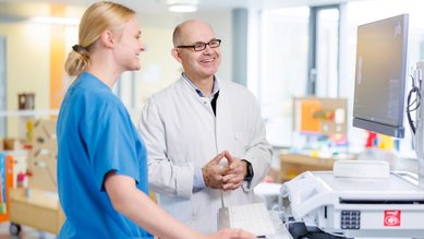 Ein Arzt und eine Krankenschwester stehen an einem Computer in einer medizinischen Einrichtung und schauen auf den Bildschirm.