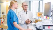 Ein Arzt und eine Krankenschwester stehen an einem Computer in einer medizinischen Einrichtung und schauen auf den Bildschirm.