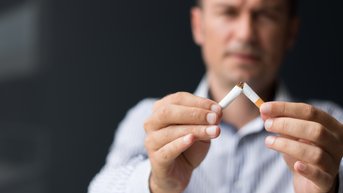 Ein Mann hält eine zerbrochene Zigarette in beiden Händen und zeigt sie nach vorne.