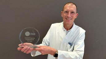 Ein Arzt in weißem Kittel hält einen Preis in der Hand, der für eine Auszeichnung in Thüringen verliehen wurde.