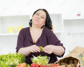 Eine Frau mit dunklen Haaren bereitet frisches Gemüse in einer modernen Küche vor, während sie Salatblätter in der Hand hält. Verschiedene Gemüsesorten sind auf der Arbeitsfläche verteilt.