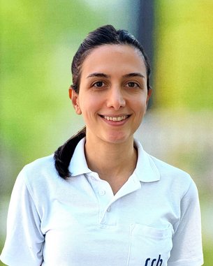 Eine Frau mit einem weißen Poloshirt steht lächelnd vor unscharfem Hintergrund. Auf dem Shirt ist "srh" aufgedruckt.