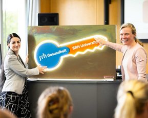 Zwei Frauen präsentieren einen großen Schlüssel mit dem Logo der SRH Universität während einer Veranstaltung.