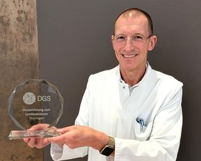 Ein Arzt in weißem Kittel hält eine Auszeichnung der DGS für das Landeszentrum Thüringen in den Händen.